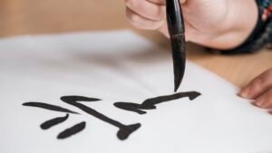 person writing a chinese character using calligraphy ink and paper