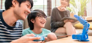 Happy Chinese son with father controlling a robot arm while mother smiles at them.