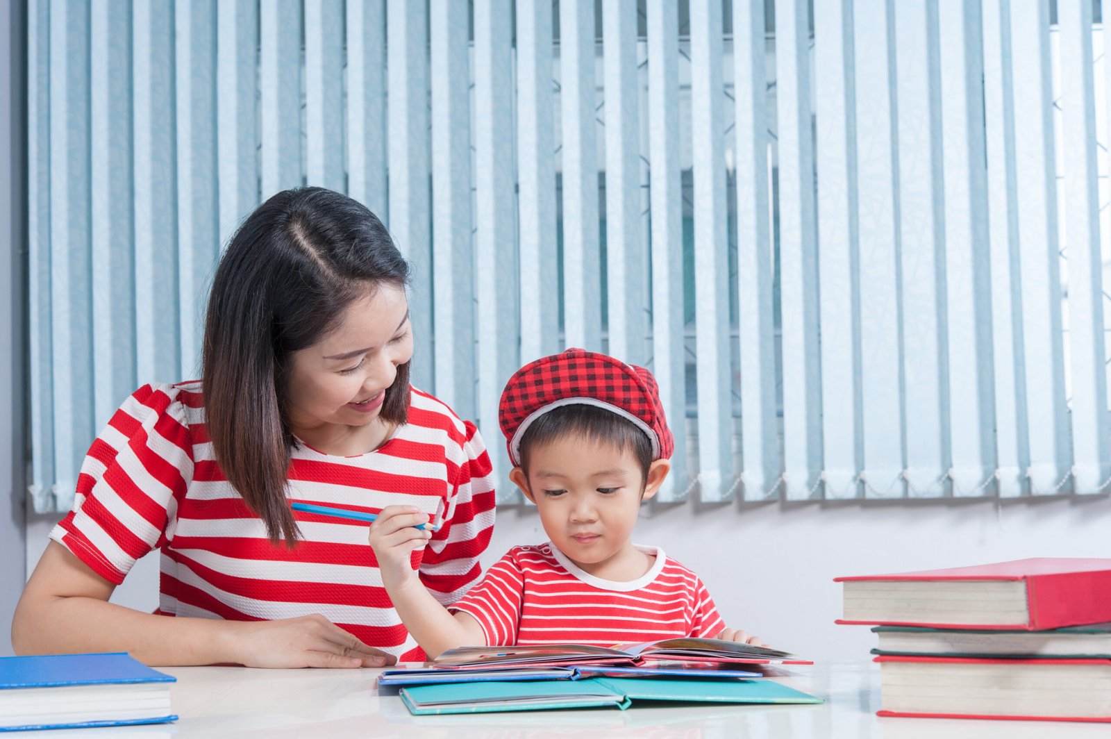 Cute boy doing his school homework with his mother, at home, he